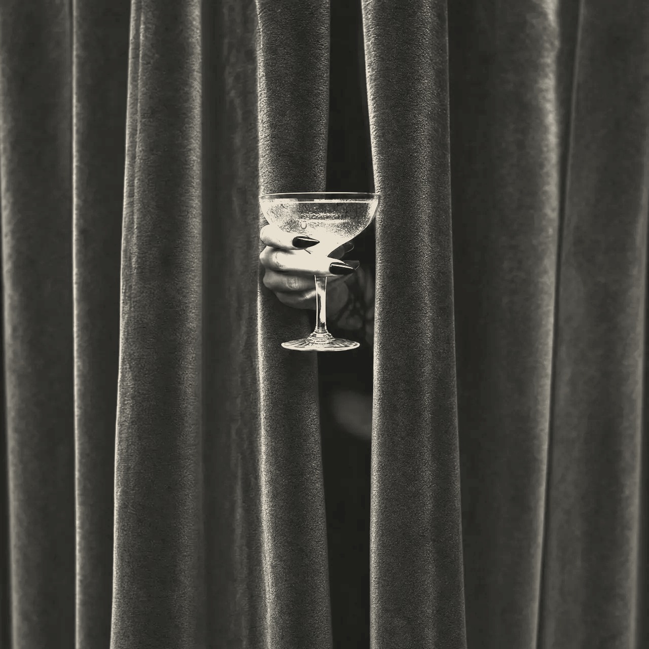 A hand holding a coupe through a velvet curtain